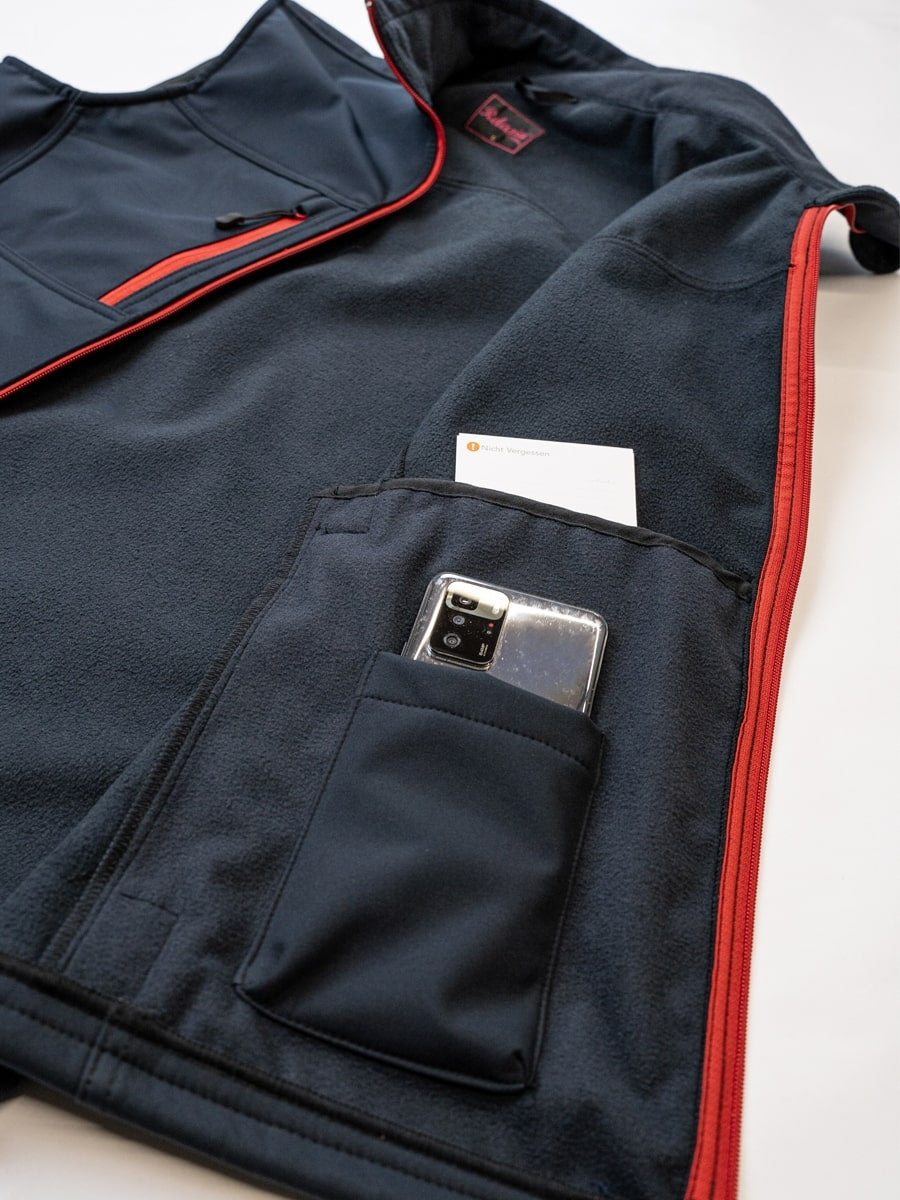 Marineblaue Softshell-Weste mit Handytasche im Innenfach und rotem Reißverschlussrand.